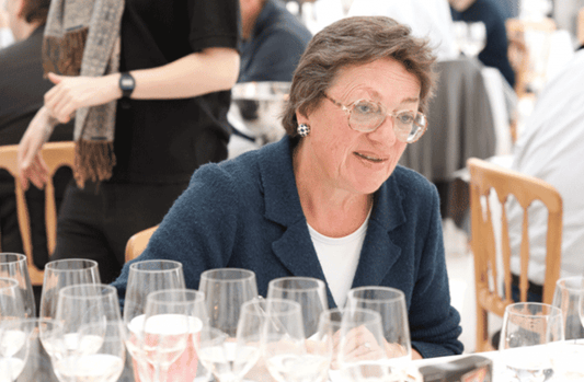 Rosemary George sits behind a table filled with wine glasses.