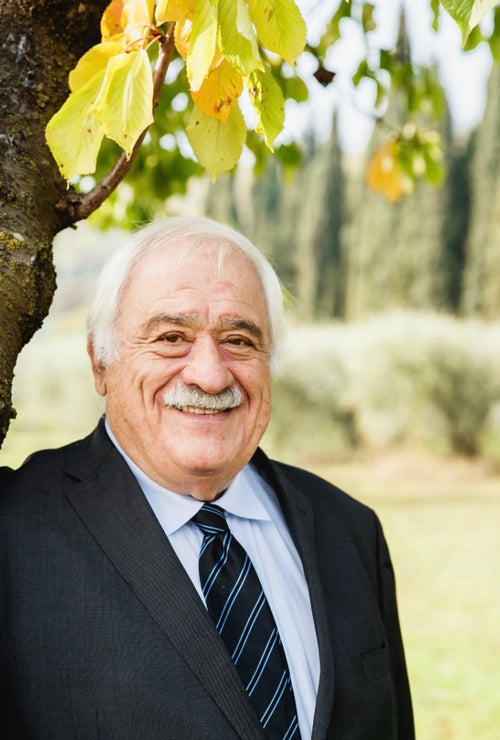 Attilio Scienza smiles at the camera with a tree branch of yellow leaves above his head