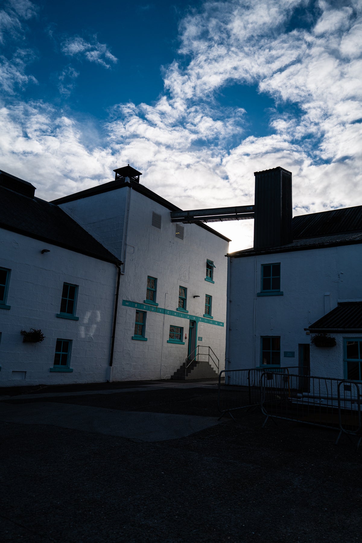 The exterior of the distillery, white buildings, with blue accents, under a cloudy blue sky