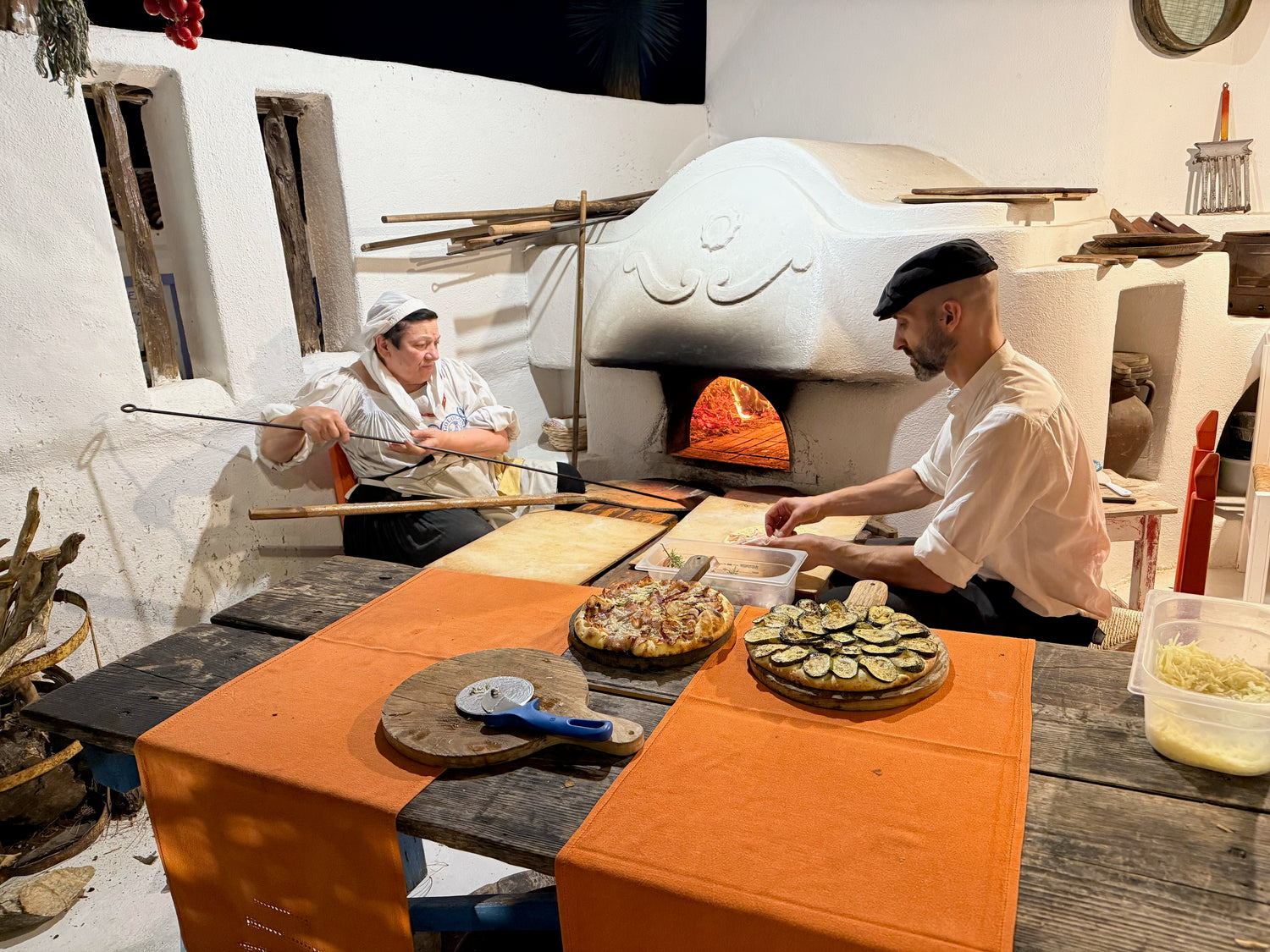 A man and woman cook at a masonry oven. 