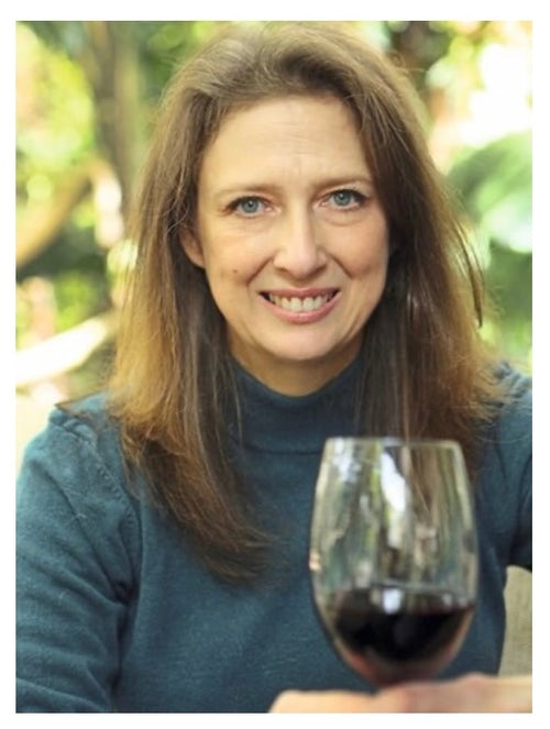 Joanne Gibson sits and smiles at the camera holding a glass of red wine with her left hand