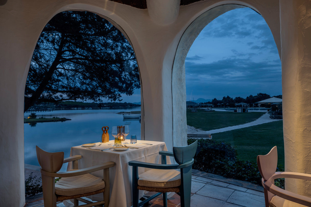 A table and chairs outdoors against an early evening sky near the water's edge.