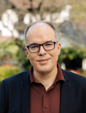 Miquel Hudin sits and smiles at the camera in a garden