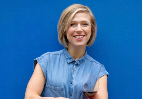 Rebecca Gibb stands with a glass of red wine behind a blue background