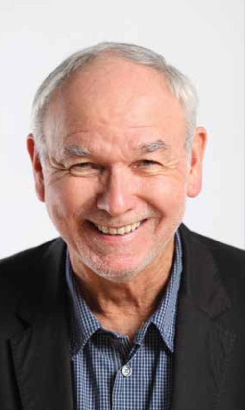 Rod Phillips sits and smiles at the camera behind a white background
