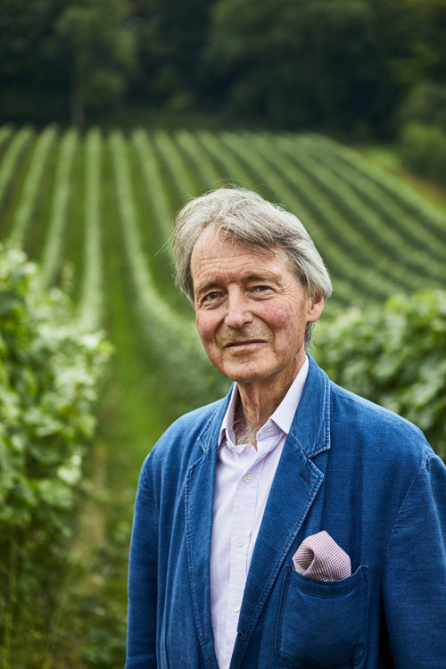 Steven Spurrier smiles at the camera standing against a bright green vineyard