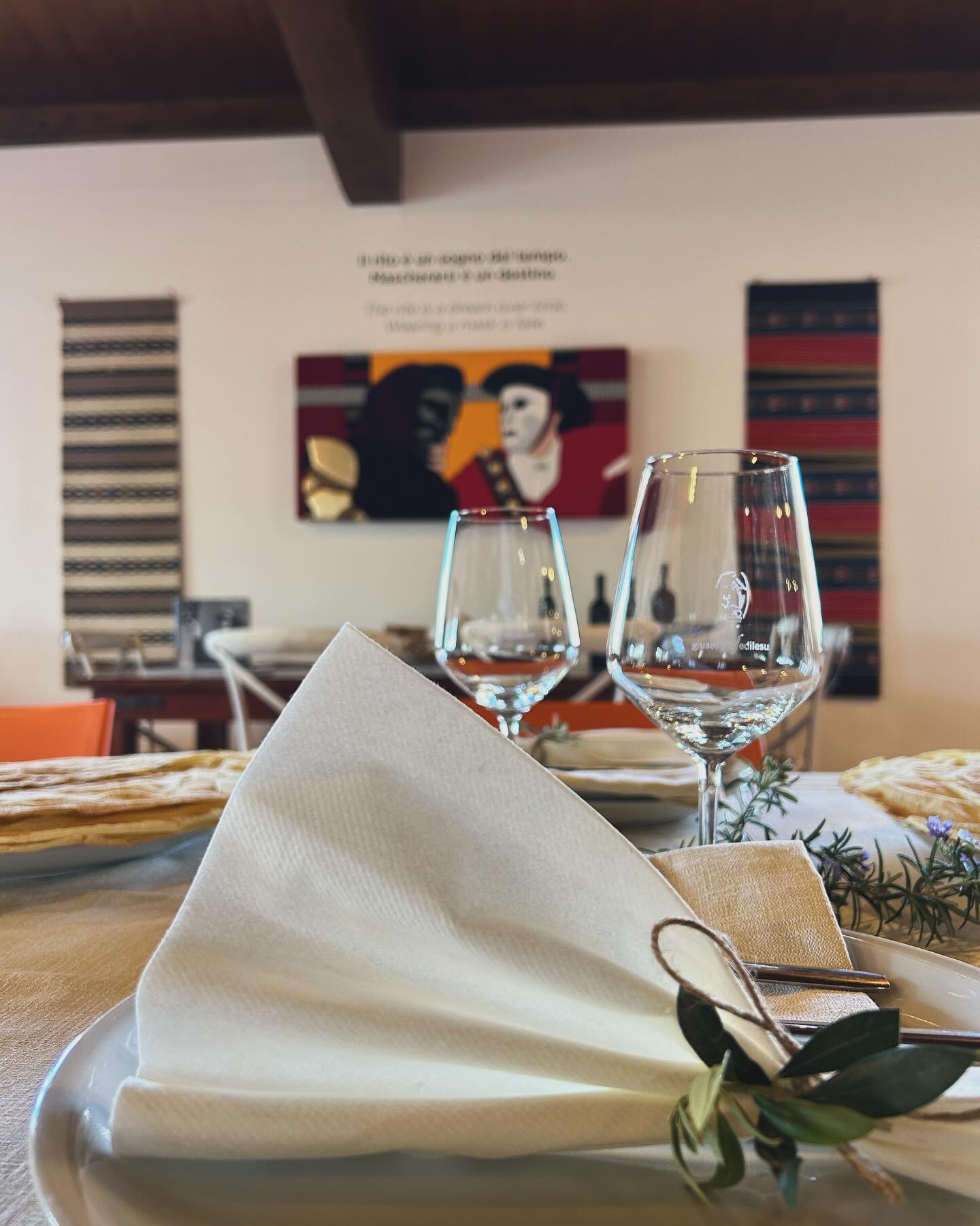 Two wine glasses and a neatly folded napkin against a white wall backdrop with colourful images and banners.